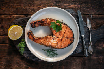 Grilled salmon steak with a lemon juice on the wooden kitchen table.