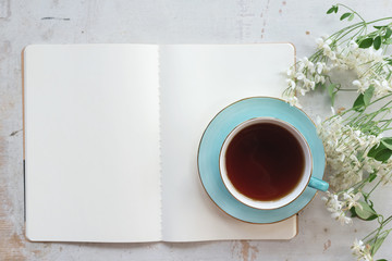 Open blank page book with a copy space and cup of tea on a white wooden table background.
