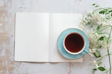 Open blank page book with a copy space and cup of tea on a white wooden table background.