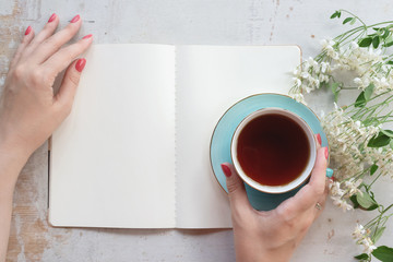 Woman is reading an open blank page book with a copy space and drinking a tea from a cup on a old...