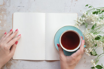 Woman is reading an open blank page book with a copy space and drinking a tea from a cup on a old...