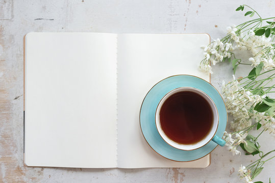 Open blank page book with a copy space and cup of tea on a white wooden table background.