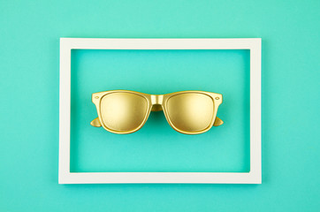 Top view of golden trendy sunglasses over the pastel turquoise background