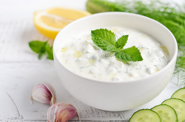 Greek dip sauce or dressing tzatziki and ingredients decorated with olive oil and mint on white wooden table 
