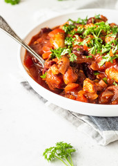 Meat stew with red beans, bell pepper and onion in tomato sauce in a white plate over light grey slate or stone background. 