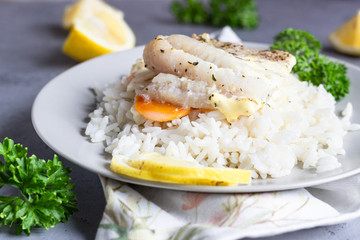 Fish baked with carrot, onion, parsley and sliced lemon on a grey plate with rice. Healthy dinner.