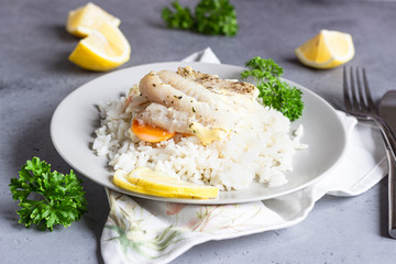 Fish baked with carrot, onion, parsley and sliced lemon on a grey plate with rice. Healthy dinner.