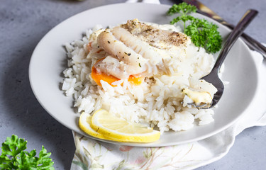 Fish baked with carrot, onion, parsley and sliced lemon on a grey plate with rice. Healthy dinner.