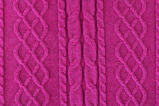 Background from a fabric texture. Wool knitted fabric with cable seamless pattern of pink-red color. Textile closeup.Openwork drawing fuchsia. Concept of example, learning of knitting,concept of cover