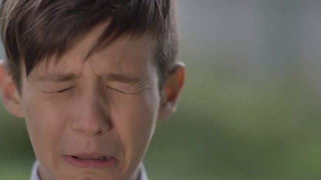 offended boy looks into the camera and starts crying, close up