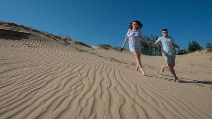 pair of young people in love run in the sand dunes.
