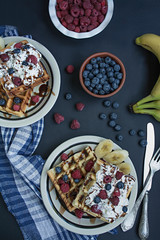 Waffles with fresh banana, raspberries, blueberries for breakfast. Belgian waffles. Dark wooden background.