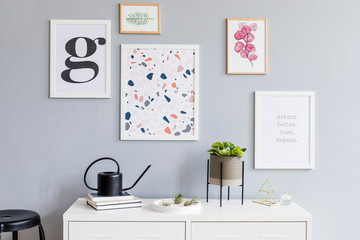 The stylish scandinavian interior of living room at nice apartment with mock up posters gallery wall, white shelf, plants, watering can. Gray background walls, wooden parquet. Modern home decor. 