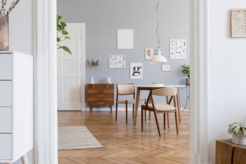 Stylish scandinavian home interior of sitting room with design wooden chairs, family table, plants, accessories and mock up posters gallery wall. Gray background walls. Modern home decor. Template.