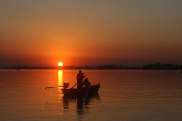 Naklejka na ściany i meble Atardecer en el rio, el barco muestra su silueta al contraste con el sol horizontal