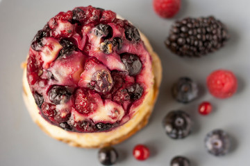 Delicious cottage cheese casserole with berries, cottage cheese pudding with berries. Appetizing fresh cottage cheese casserole with blueberries, raspberries and blackberries on a  gray background.