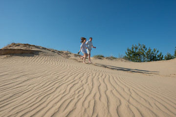 Fototapeta na wymiar pair of young people in love run in the sand dunes.