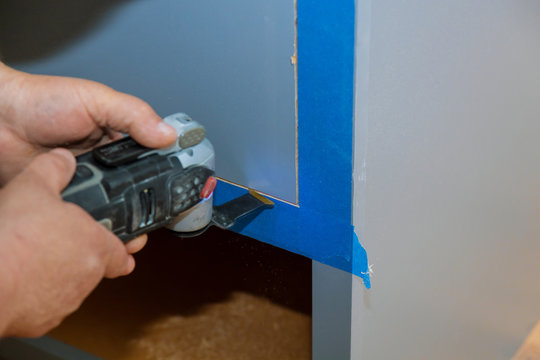 Contractor Using Oscillating Multi Functional Cutting Tool For Handyman Cut Hole In Kitchen Furniture