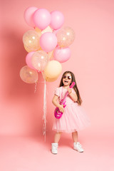 Laughing fashion little girl having fun with guitar isolated on pink background.