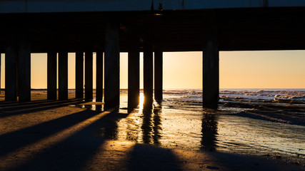 Sunrise through ocean pier on beach