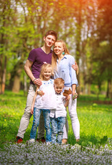 Fototapeta premium Portrait of family having fun in flowering city park on bright sunny day happily spending their leisure time together outdoors