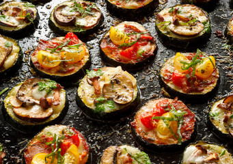 Small pizzas, Zucchini pizza bites from zucchini slices with the addition of brown mushrooms, mushroom chanterelles, mozzarella cheese, salami sausage, cherry tomatoes and herbs on a black background