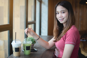 Beautiful Asian Woman in coffee shop, looking at camera, with iced cappuccino and matcha green tea