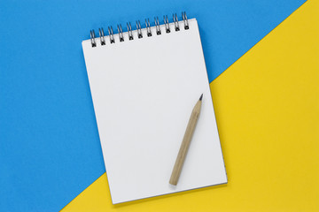 Open spiral notebook with a blank page on a blue and yellow background, next to a pencil