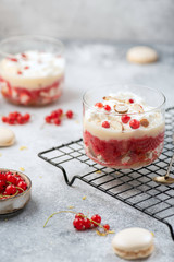 trifle with red currant and whipped cream, custard  in glasses on grey background on stand