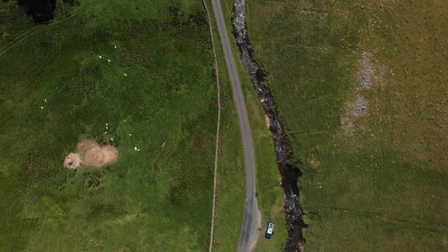High-altitude aerial shot looking down at 90 degrees to the stream running through Barbon Beck Valley, Carnforth, England. This countryside footage shows a stream running alongside a country lane.