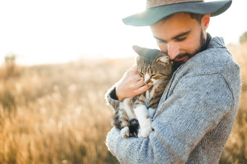 Lovely young hipster with a cat. A guy with a mustache and a beautiful smile is hugging a cat....