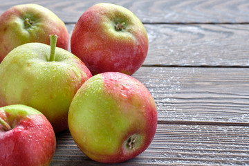 fresh harvest apples on brown wet natural old wooden table surface. Fruits are covered by raindrops.