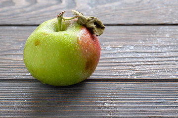 Red green apple, covered by raindrops on wooden table