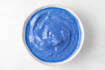 nice cream or smoothie bowl made of blue spirulina, frozen bananas and berries on white marble tabl