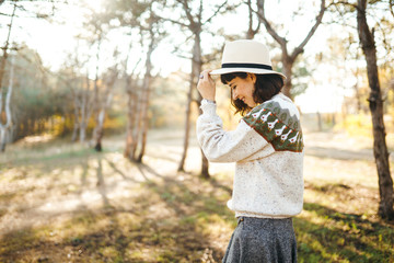 Lovely girl with a beautiful smile at sunset in the forest. The girl is dressed with a hat, a light sweater and a skirt. Knee-high boots. Hipster girl concept, lifestyle style, autumn style.