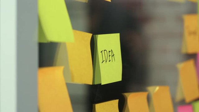 Asian creative man stick a sticky note on glass board. Young professional business male write information, strategy, reminder on paper, business situation, startup in Loft office concept. Slow motion.