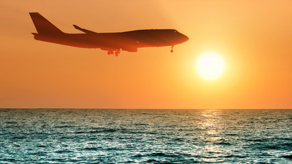 Fototapeta na wymiar airplane flying over sea water on sunset sky background side panorama landscape view of passenger jet plane landing and setting sun reflection on ocean water air travel aircraft silhouette wallpaper
