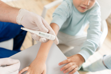 Male arm hold electronic thermometer showing high temperature. Pediatrician in the hospital