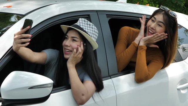 Happy Two asian women taking a picture of yourself with smart phone in the car on the road. Natural background sunlight, daylight and tree. summer holiday travel trip concept