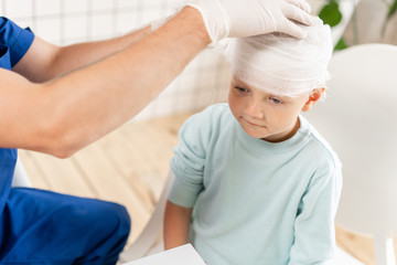 Fototapeta premium Doctor bandaged a boy head with trauma in his head and elastic bandaged around his head