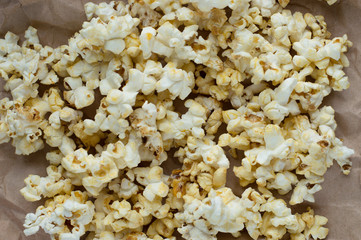 Homemade vegan fresh crunchy popcorn on brown craft paper lie on a dark wooden table. A useful snack for a movie, an idea for a meal. Close-up, top view.