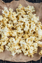 Homemade vegan fresh crunchy popcorn on brown craft paper lie on a dark wooden table. A useful snack for a movie, an idea for a meal. Dark mood background, top view.