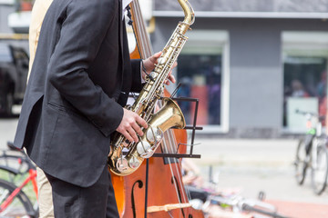Street musician's hands playing saxophone and double-bass in an urban environment.