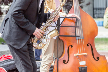 Street musician's hands playing saxophone and double-bass in an urban environment.