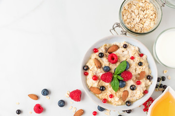 oatmeal porridge with fresh berries, nuts, honey and mint in a bowl for healthy diet breakfast. top view