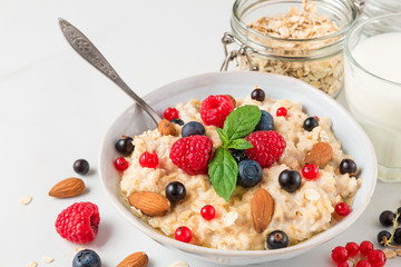 oatmeal porridge with fresh berries, nuts, honey, mint in a bowl with glass of milk for healthy diet breakfas