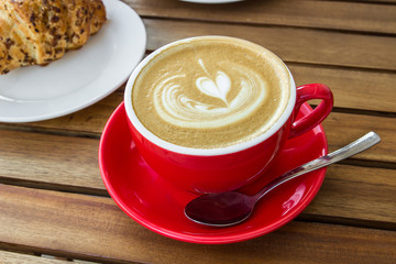 Red cup of cappuccino with croissant on a table in an outdoor cafe. Tipical italian breakfast. Selective focus