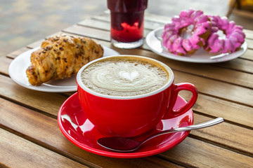 Red cup of cappuccino with croissant on a table in an outdoor cafe. Tipical italian breakfast....