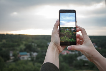 Close-up of female hands shoot a beautiful landscape with green hills and sunset on a smartphone, selective focus