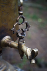 Close-up graceful faucet of an old copper samovar on a blurred forest background, selective focus